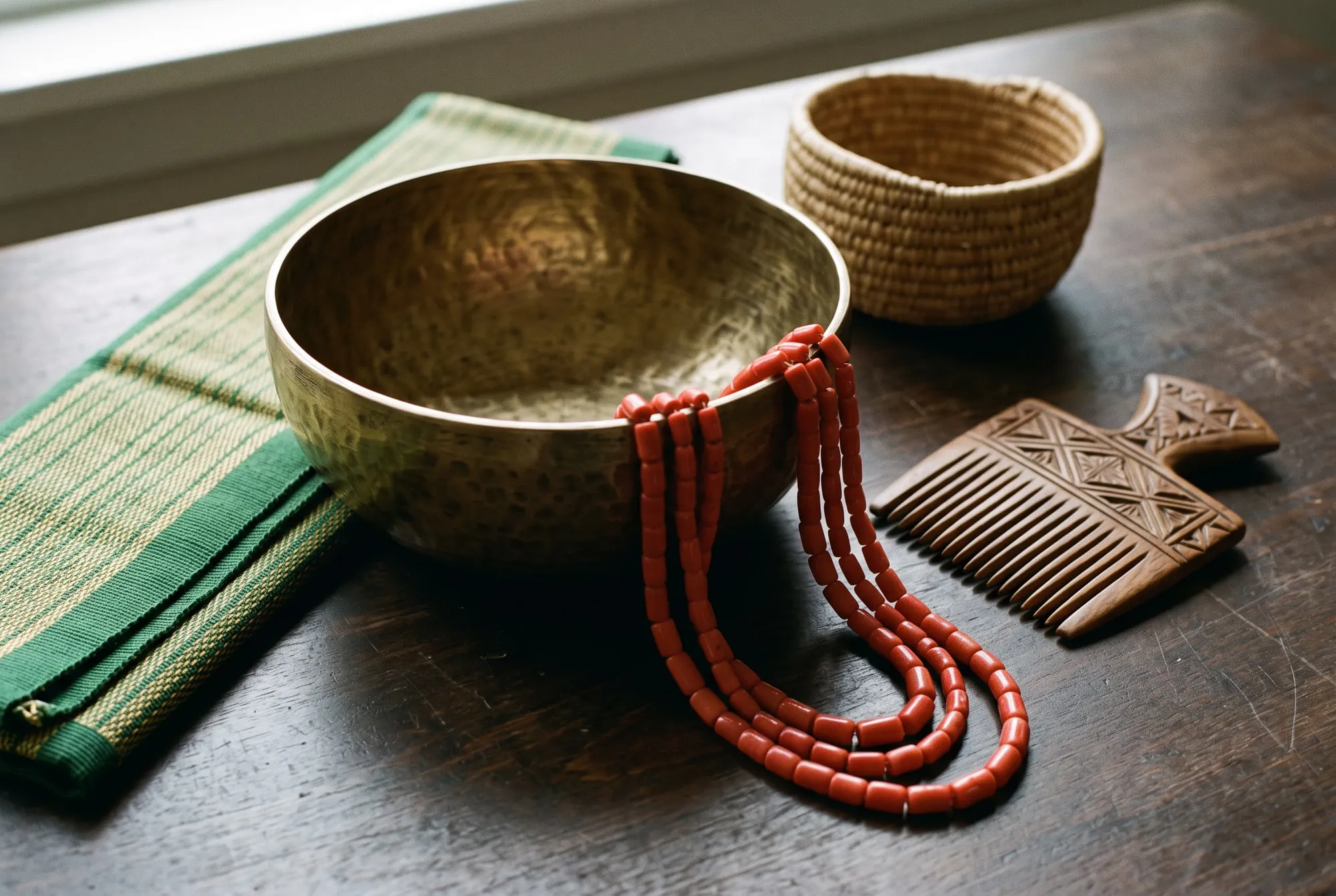 Nigerian craft objects: a hammered brass bowl, coral beads, a carved comb and a woven basket