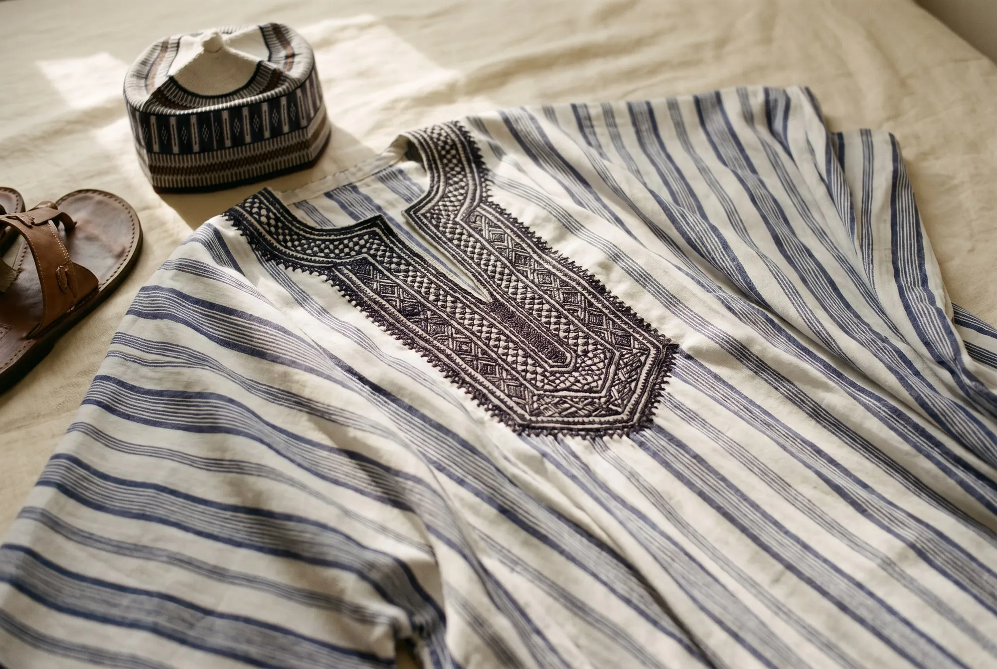 A Nigerian robe with dense hand-worked embroidery at the neckline, beside an embroidered cap