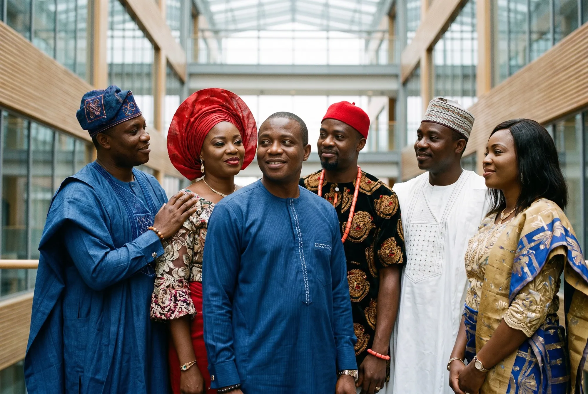 Nigerians from several ethnic groups standing together in traditional dress: agbada and fila, gele, isiagu with a red cap and coral beads, an embroidered babban riga, and a george wrapper